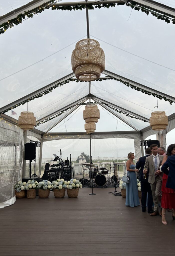Clear-top tent with woven pendant lights, greenery garland and a band setup