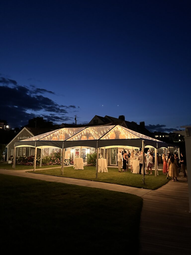 Frame tent glowing at night as guests mingle inside