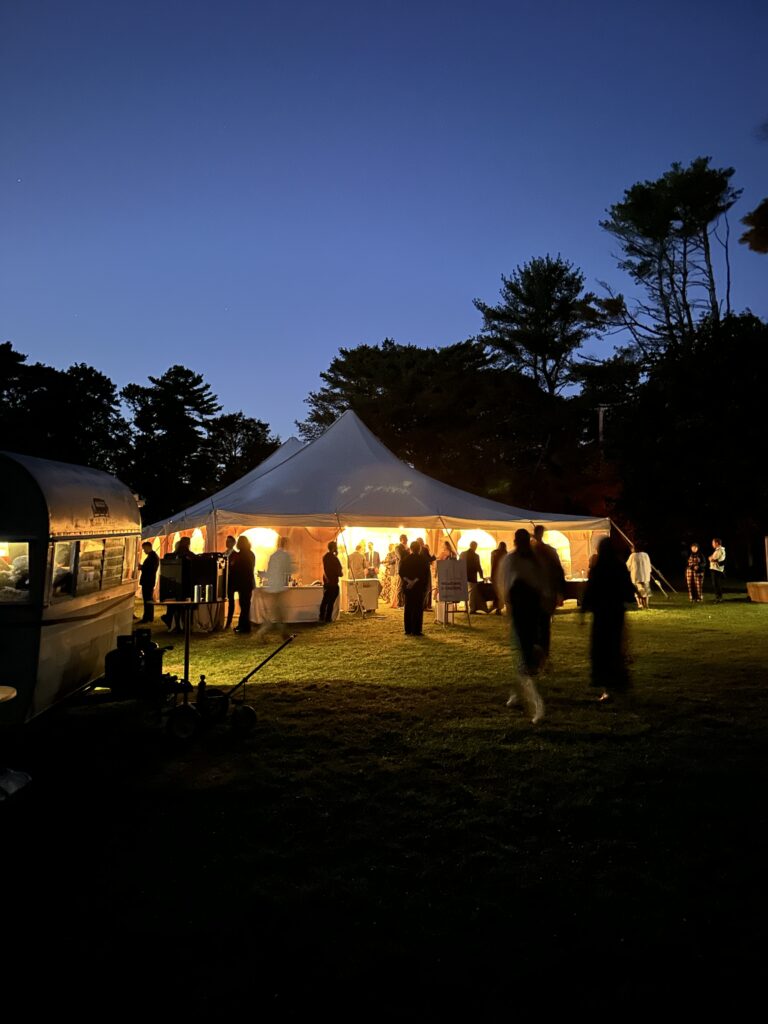 Guests gathering outside a lit tent after sunset